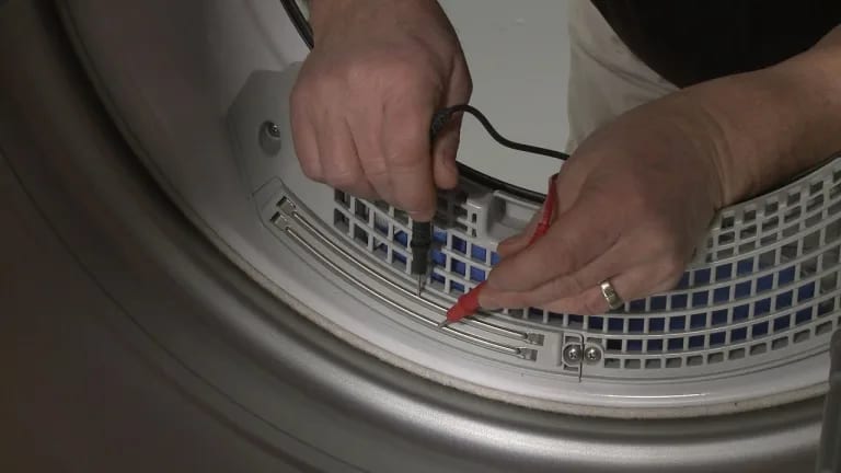 a picture of two hands measuring dryer wetness sensor resistance with multimeter leads